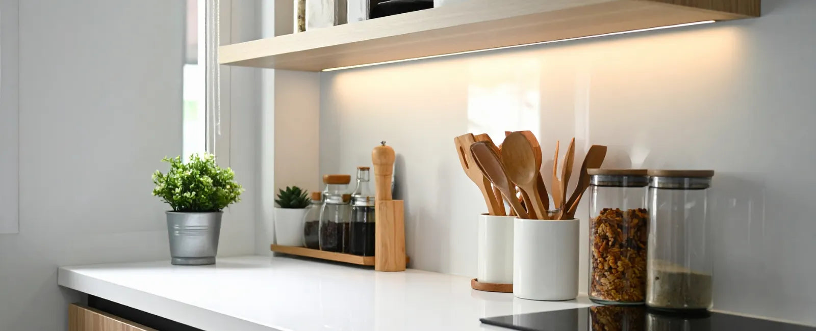 Clean modern kitchen countertop with organized utensils and jars under cabinet lighting