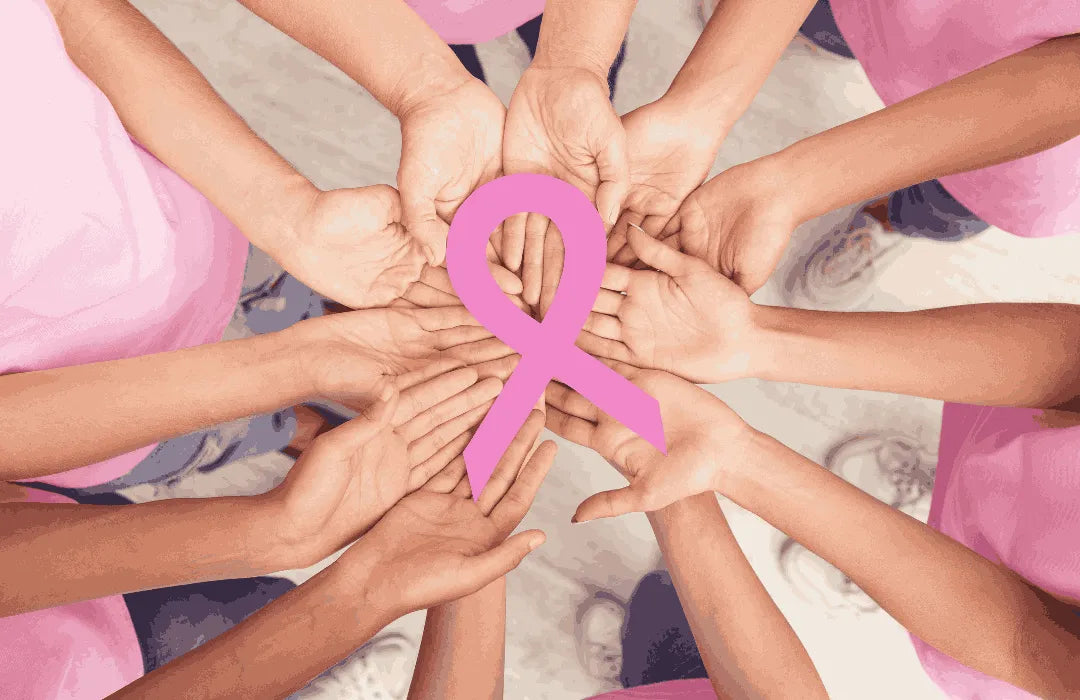 Group of people joining hands around a pink breast cancer awareness ribbon, symbolizing unity and support.