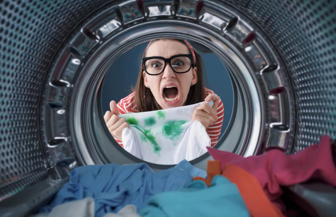 Person wearing glasses holding a stained shirt while looking inside a washing machine.