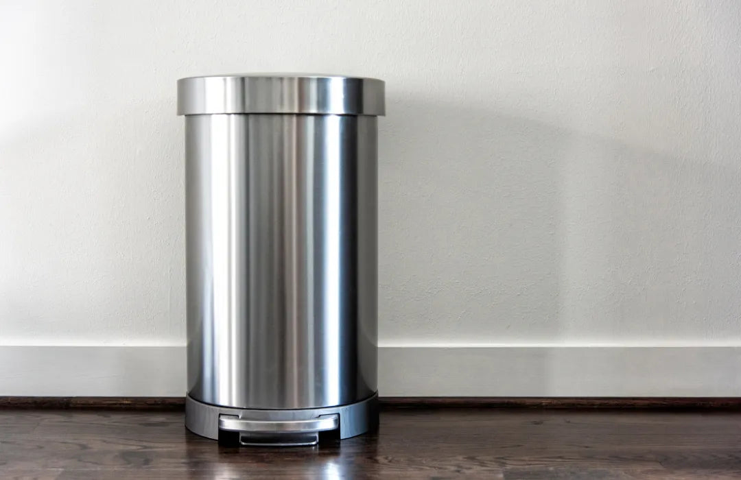 Stainless steel trash can on a wooden floor against a white wall
