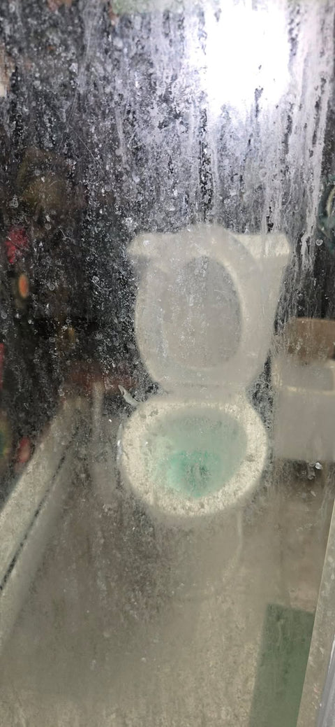 Spotted glass so cloudy the toilet behind it is blurry